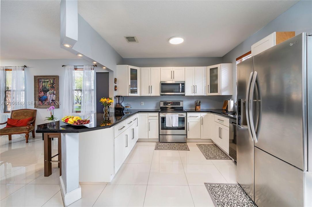 Kitchen featuring white shaker-style cabinetry, dark stone countertops, stainless steel appliances, and polished tile flooring