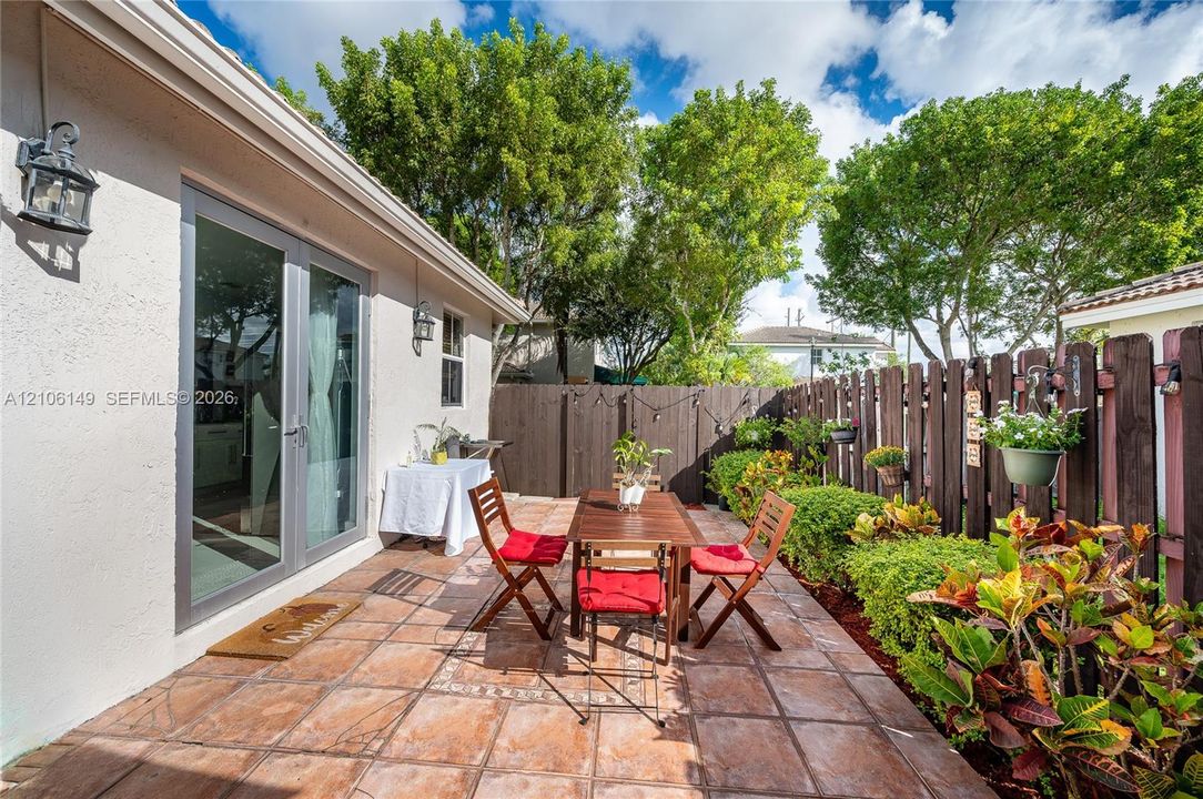 Tiled outdoor patio featuring a stained wood privacy fence, wall-mounted exterior lanterns, and established landscaping