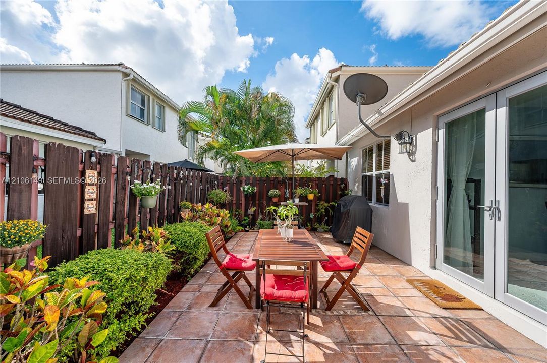 Paved rear patio featuring a wood-style privacy fence, wall-mounted exterior lighting, and double-glass door entry