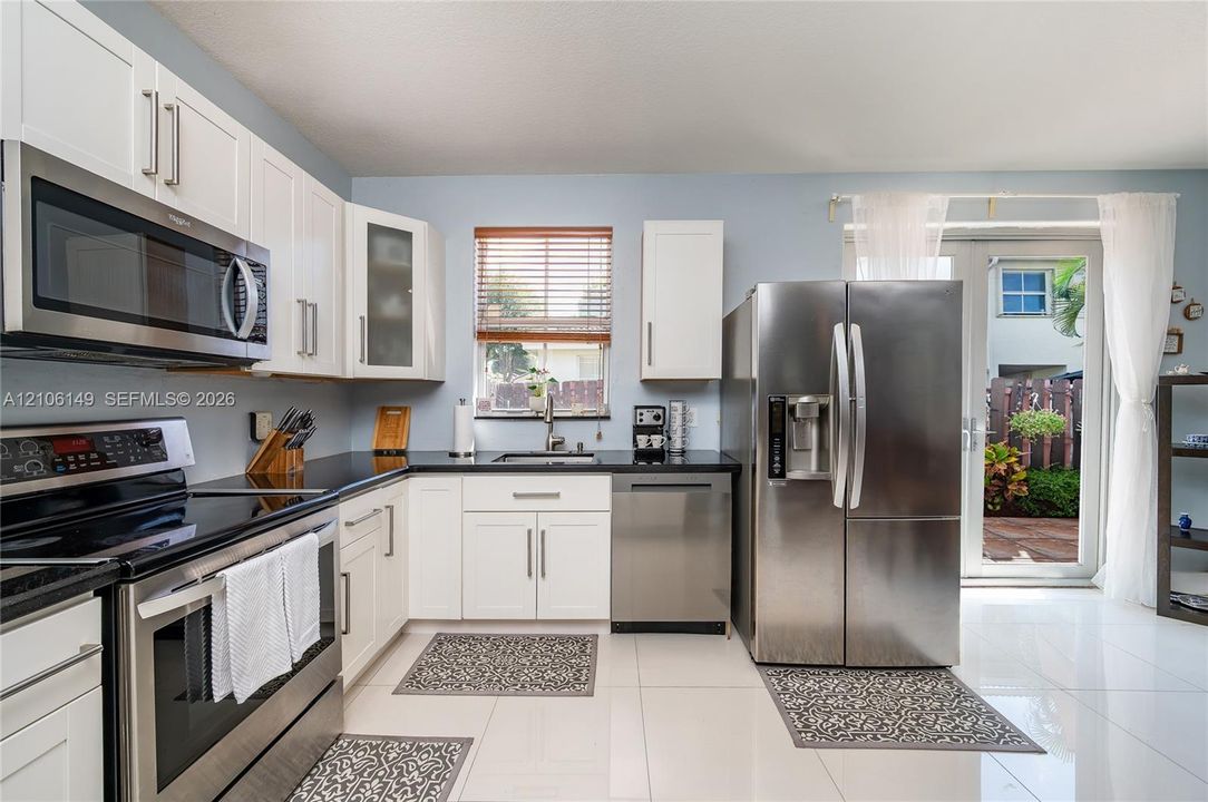 Kitchen featuring white shaker-style cabinetry, dark stone countertops, stainless steel appliances, polished tile flooring, and double glass doors