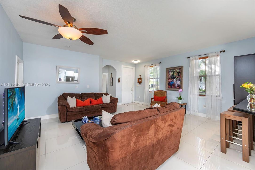 Living area featuring polished tile flooring, a five-blade ceiling fan with integrated light fixture, and an arched doorway