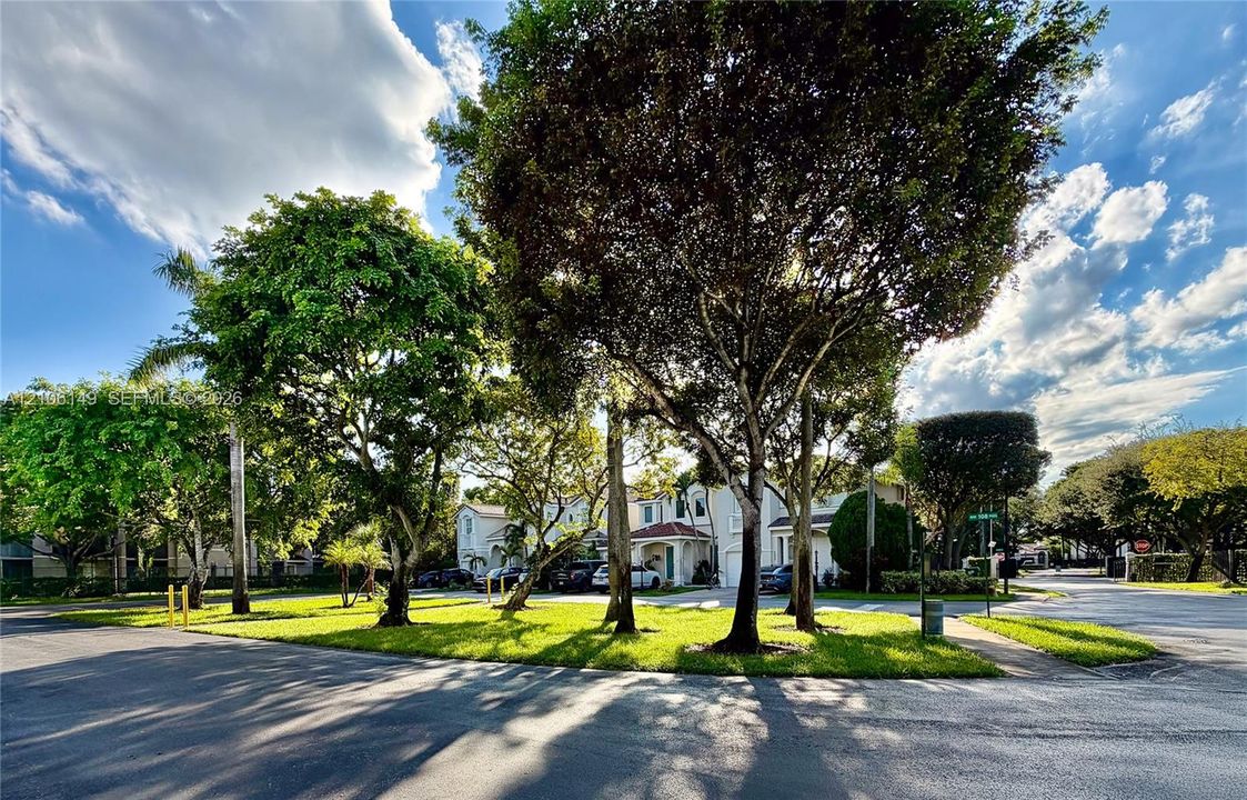 Expansive green space featuring mature trees and established landscaping surrounding a multi-level residential structure with a covered entrance