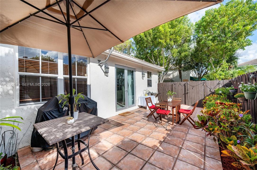 Private patio featuring ceramic tile flooring, privacy fencing, and exterior wall-mounted lighting