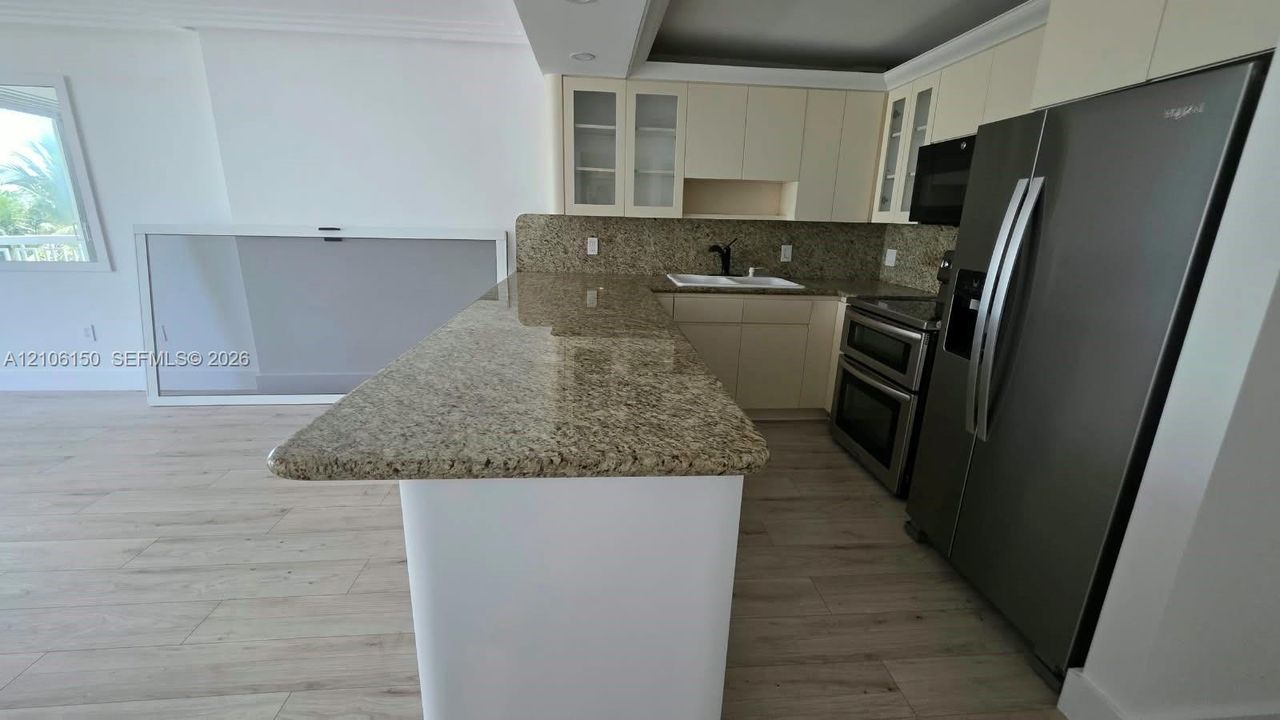 Kitchen featuring an expansive stone countertop, stainless steel appliances, light-toned cabinetry, and wood-finish flooring