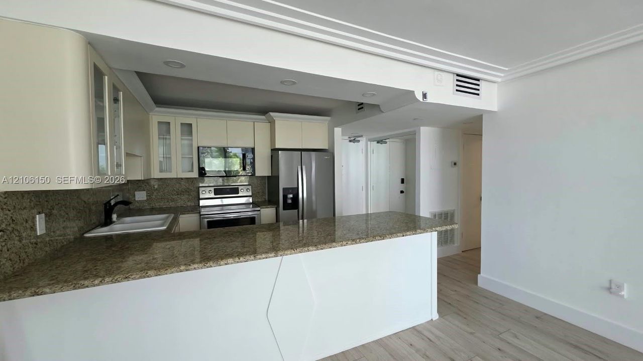Kitchen featuring stone countertops, breakfast bar, stainless steel appliances, upper cabinetry with glass-panel doors, and wood-finish flooring