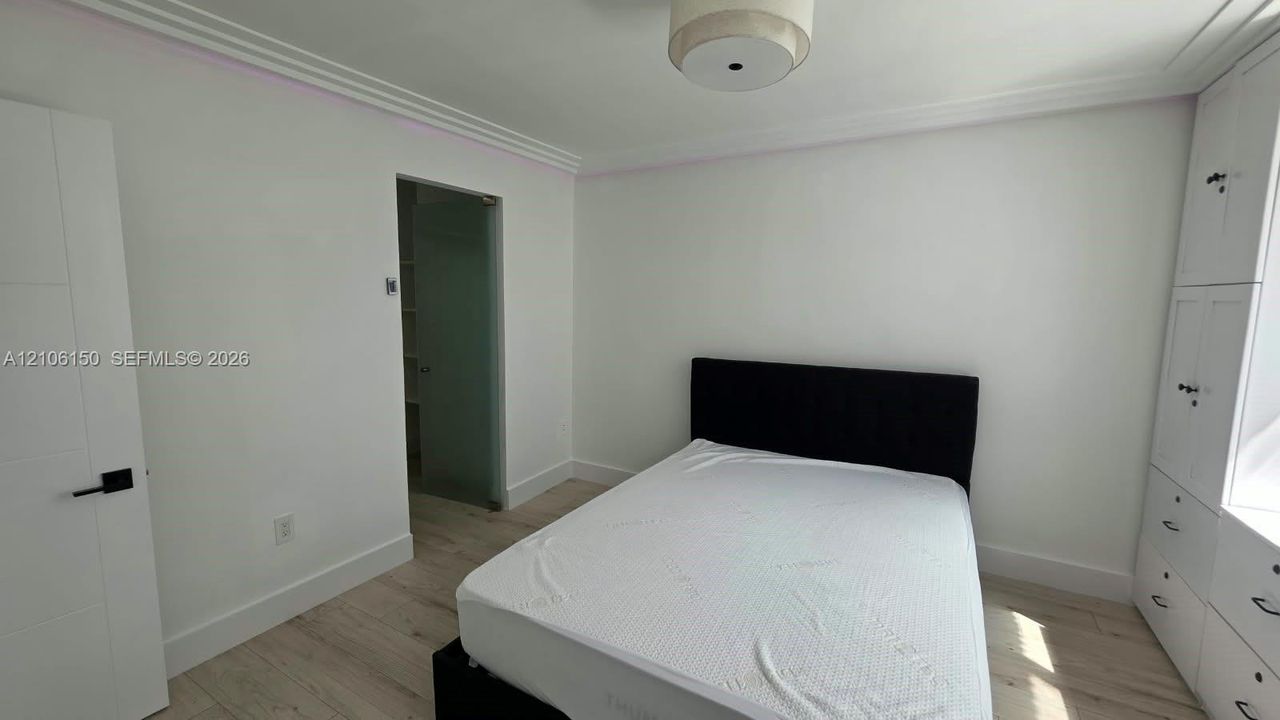 Room featuring wood-finish flooring, crown molding, built-in floor-to-ceiling cabinetry, a flush-mount drum ceiling light, and a door with matte black hardware