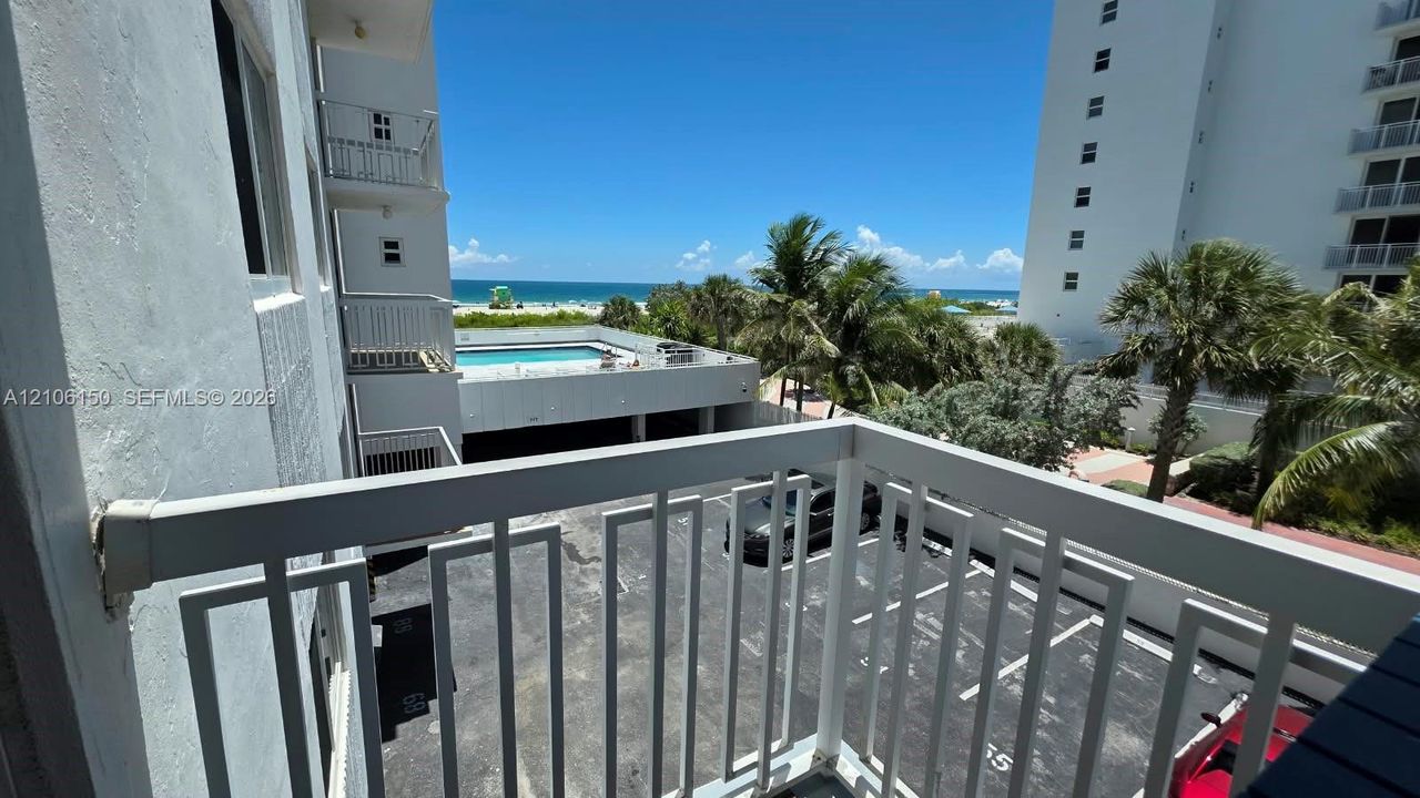 Balcony with metal railing overlooking the pool, parking area, and oceanfront horizon