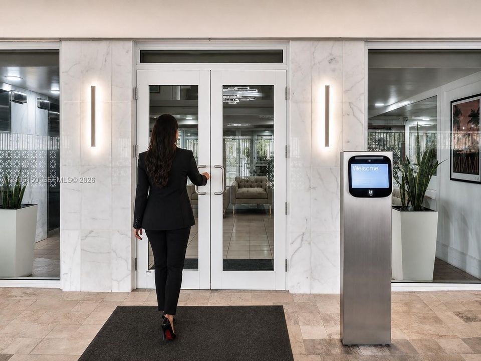 Double glass entry doors with metallic hardware, flanked by floor-to-ceiling stone-clad pillars, vertical wall-mounted lighting fixtures, and a secure electronic access terminal