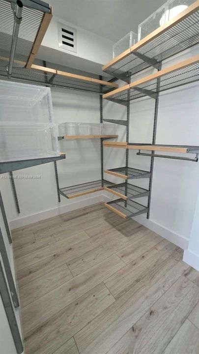 Walk-in closet featuring adjustable metal wire shelving, wood-trim edging, and wood-finish flooring