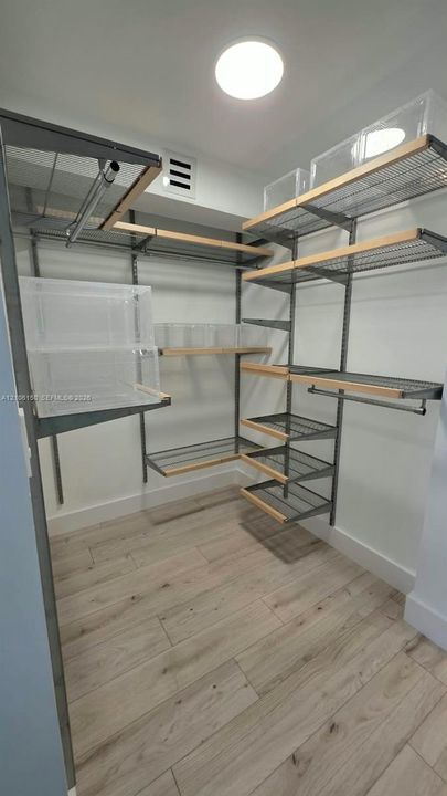 Storage space featuring adjustable metal wire shelving, integrated wood-trim detailing, dual hanging rods, and wood-finish tile flooring