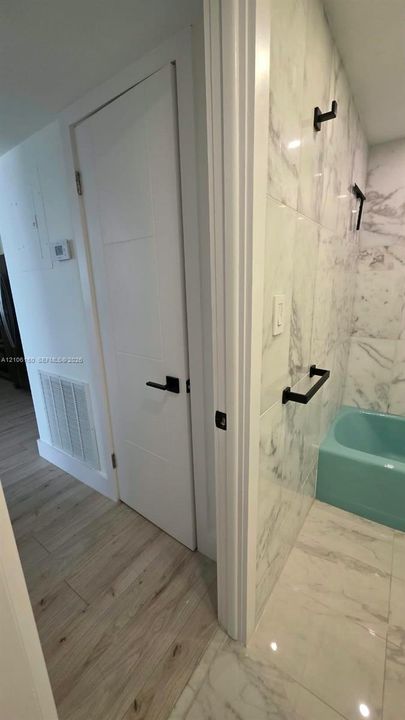 Large-format stone-pattern tile flooring and shower surround, featuring matte black hardware and a contemporary interior door with a matching black lever handle