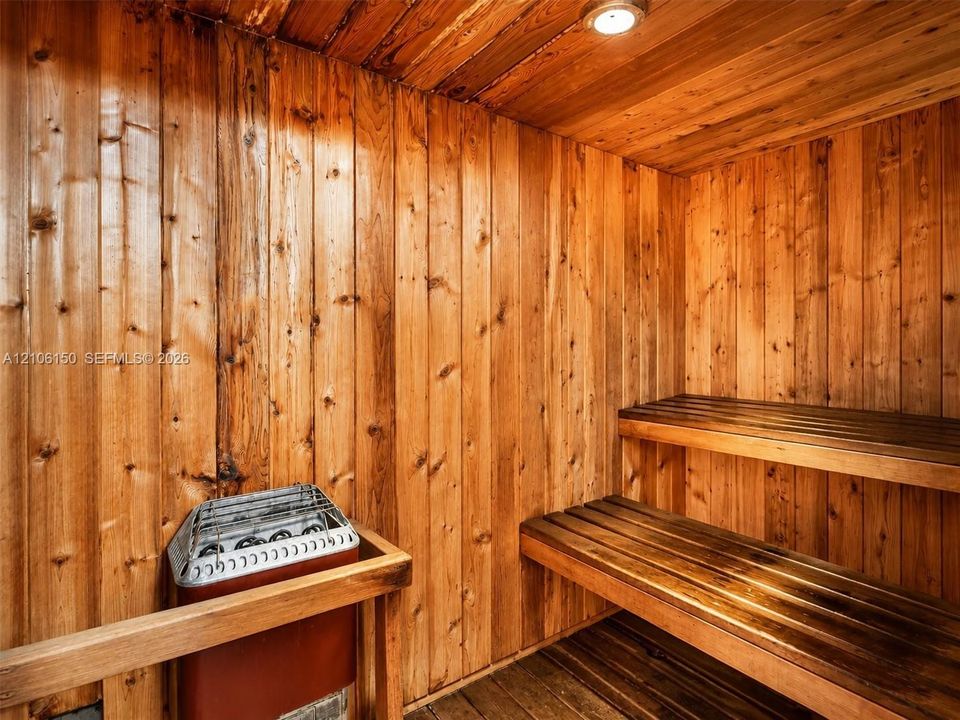 Sauna room featuring vertical wood wall paneling, multi-level wood bench seating, and an integrated heating unit