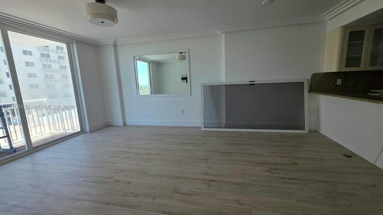 Living area featuring wood-finish flooring, sliding glass balcony door, recessed ceiling lighting, wall-mounted mirror, and stone-surface breakfast bar