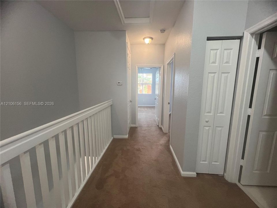 Hallway featuring neutral carpet flooring, white paneled interior doors, and a white balustrade with a horizontal handrail