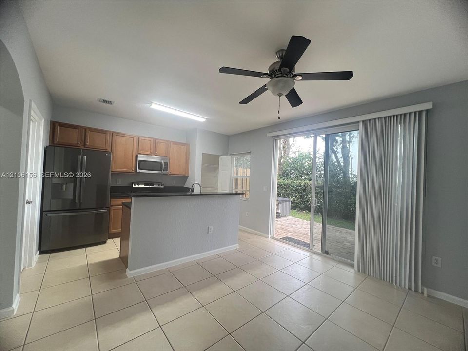 Kitchen featuring wood cabinetry, dark-toned countertop, stainless steel appliances, tile flooring, and sliding glass doors