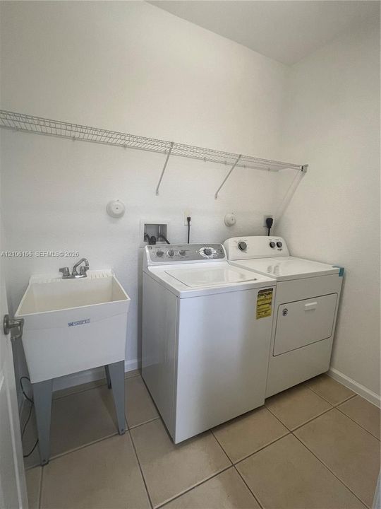 Laundry area featuring ceramic tile flooring, a utility sink with a chrome faucet, and wire wall shelving