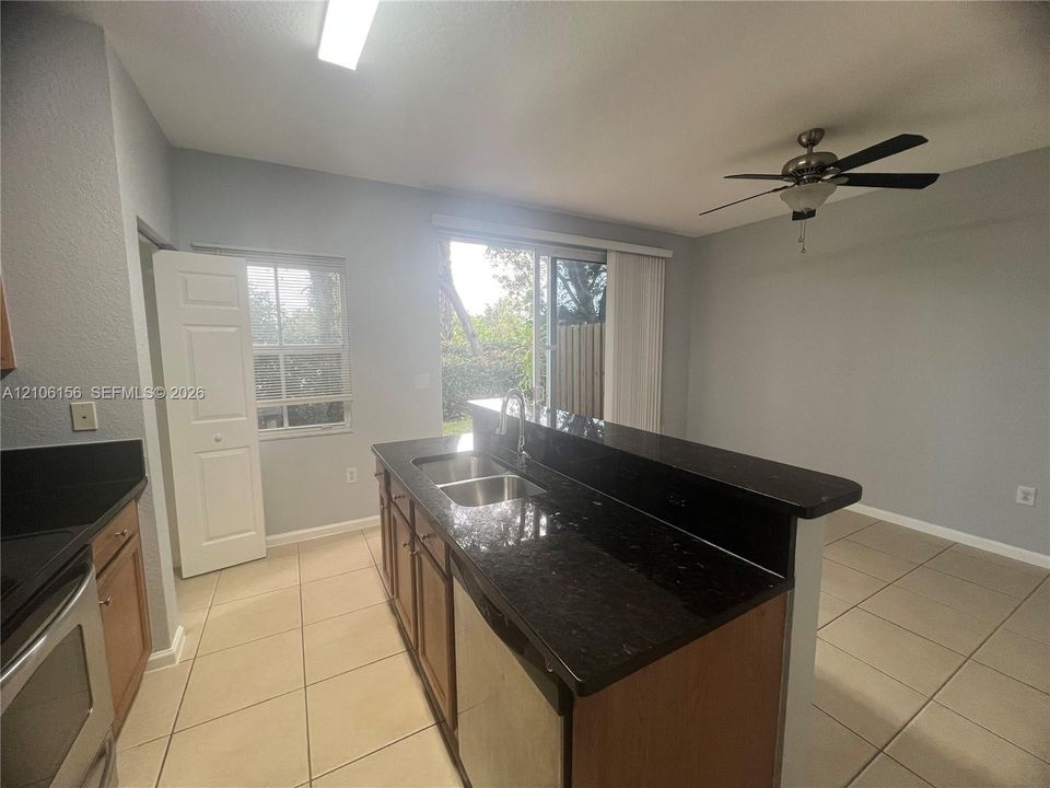 Kitchen featuring an island with a dual-basin sink, dark stone-finish countertops, wood-finish cabinetry, tile flooring, and a ceiling fan