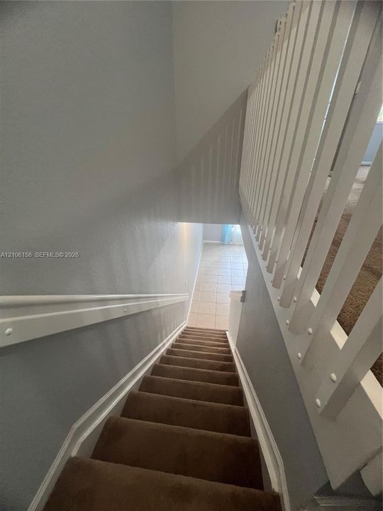 Staircase featuring neutral carpeted treads, a white wooden handrail, and a vertical balustrade