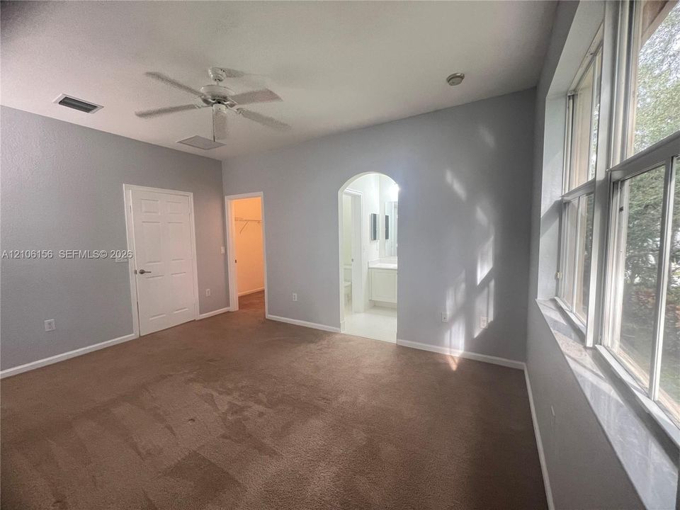 Spacious room featuring carpeting, a ceiling fan, an arched entryway, and multiple tall windows