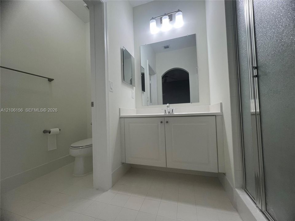 Floating vanity with white cabinetry and solid-surface countertop, rectangular wall mirror, three-bulb vanity lighting, and walk-in shower enclosure