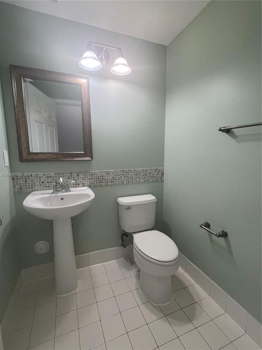 Pedestal sink with chrome faucet, wall-mounted mirror with wood-finish frame, mosaic tile backsplash, dual-light vanity fixture, and tiled flooring