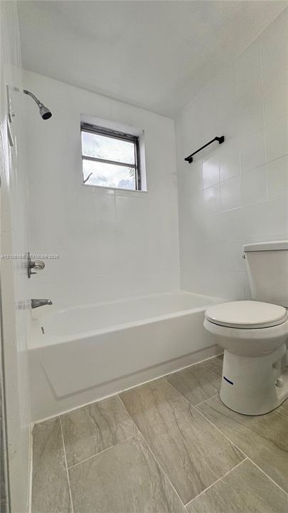 Bathroom featuring white wall tiling, a built-in tub with a shower head, ceramic tile flooring, and a matte black towel bar