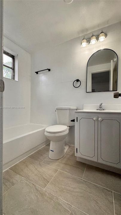 Bathroom featuring tile flooring, a white vanity cabinet with a neutral countertop, an arched wall-mounted mirror, and a three-light vanity fixture
