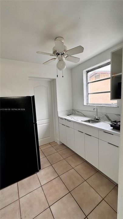 Kitchen featuring flat-panel white cabinetry, stone-patterned backsplash, square tile flooring, and ceiling fan with integrated lighting