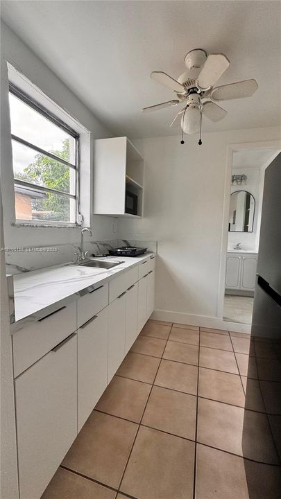 White cabinetry with minimalist hardware, stone-finish countertops, stainless steel undermount sink, multi-pane window, and ceramic tile flooring