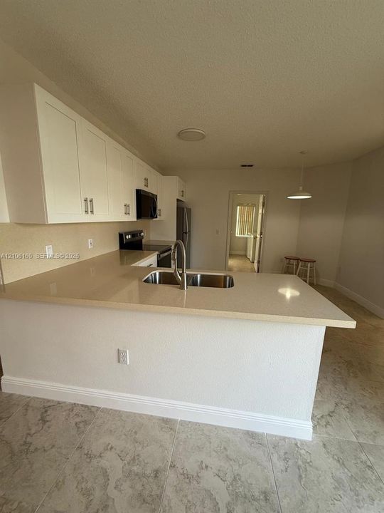 Kitchen featuring white cabinetry, solid-surface countertops, dual-basin stainless steel sink with gooseneck faucet, and tile flooring