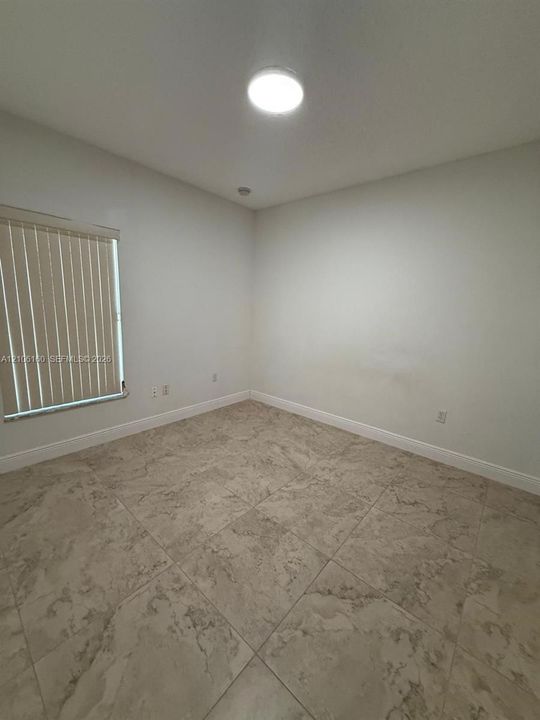 Neutral interior space featuring stone-style tile flooring, a window with vertical blinds, and a flush-mount ceiling light fixture