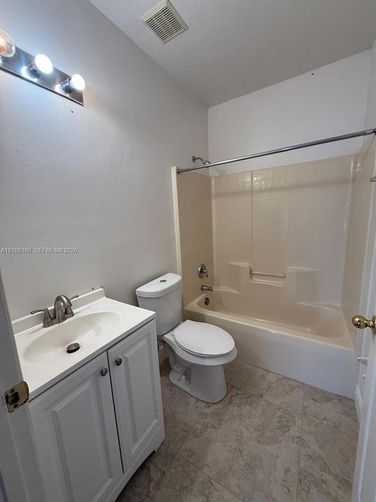 Bathroom featuring a white vanity cabinet with an integrated basin, brushed nickel faucet, wall-mounted three-light fixture, and a molded acrylic tub-shower combination