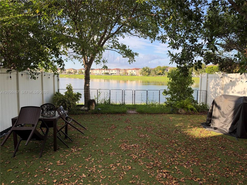 Backyard featuring a waterfront location, white vinyl privacy fencing, mature trees, and a metal perimeter fence