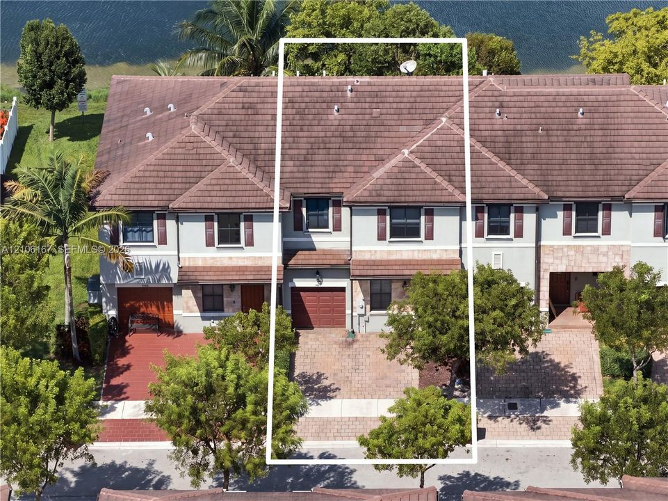 Multi-story townhome exterior featuring a paver driveway, single-car garage, earth-toned roof tiles, and decorative window shutters