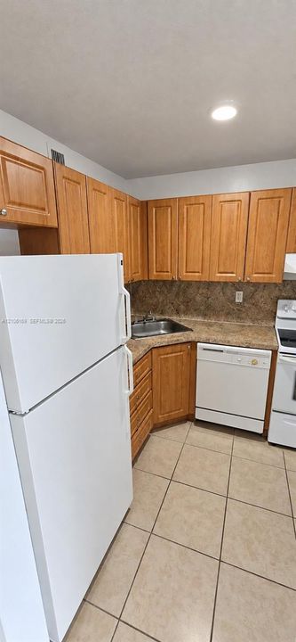 Kitchen featuring light-tone wood cabinetry, stone-finish countertops, tile flooring, and white appliances