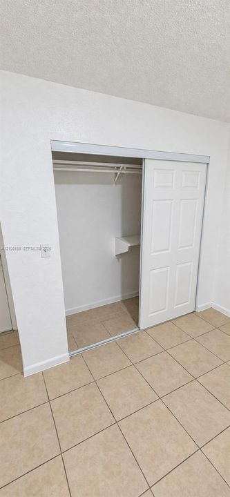 Closet featuring dual sliding six-panel doors, integrated shelving, and a hanging rod, finished with neutral tile flooring