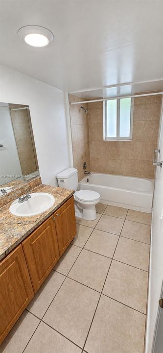 Bathroom featuring a vanity with stone-finish countertop, integrated sink, tile flooring, bathtub with tiled surround, and recessed ceiling lighting