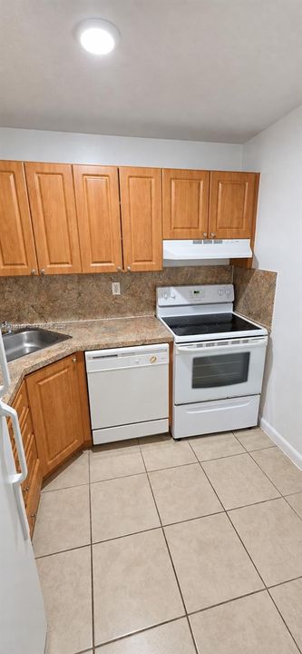 Kitchen featuring wood cabinetry, solid-surface countertops, tile flooring, and white built-in appliances including a dishwasher and electric range
