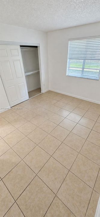 Room featuring neutral-toned tile flooring, light-colored walls, sliding closet doors, and a window with horizontal blinds