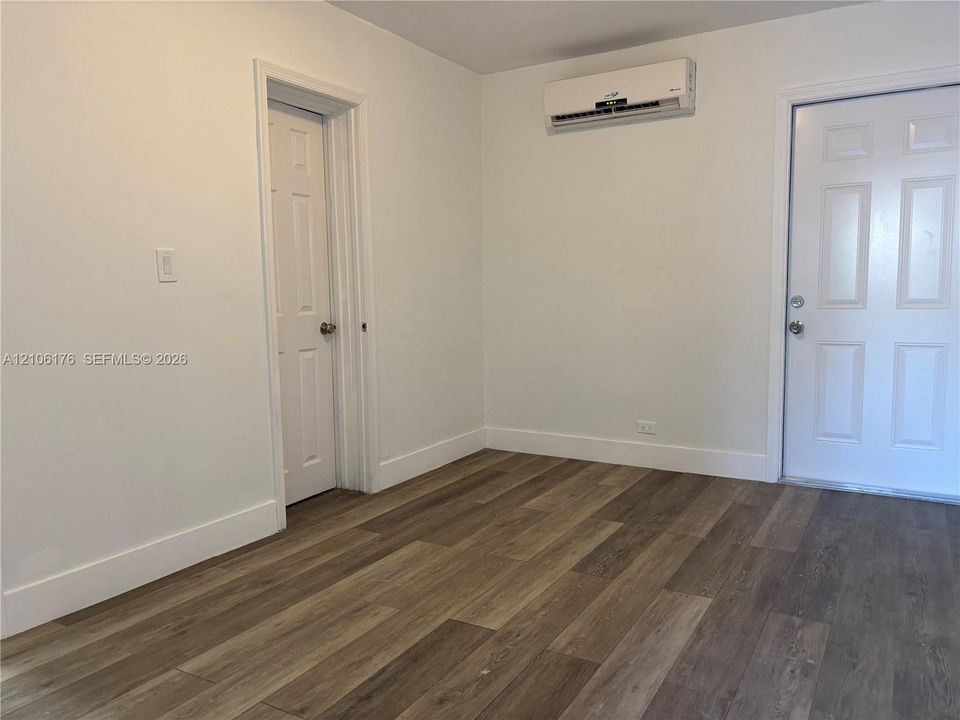 Interior space featuring wood-finish flooring, a wall-mounted ductless mini-split HVAC unit, a six-panel door, and an exterior door with dual deadbolt hardware