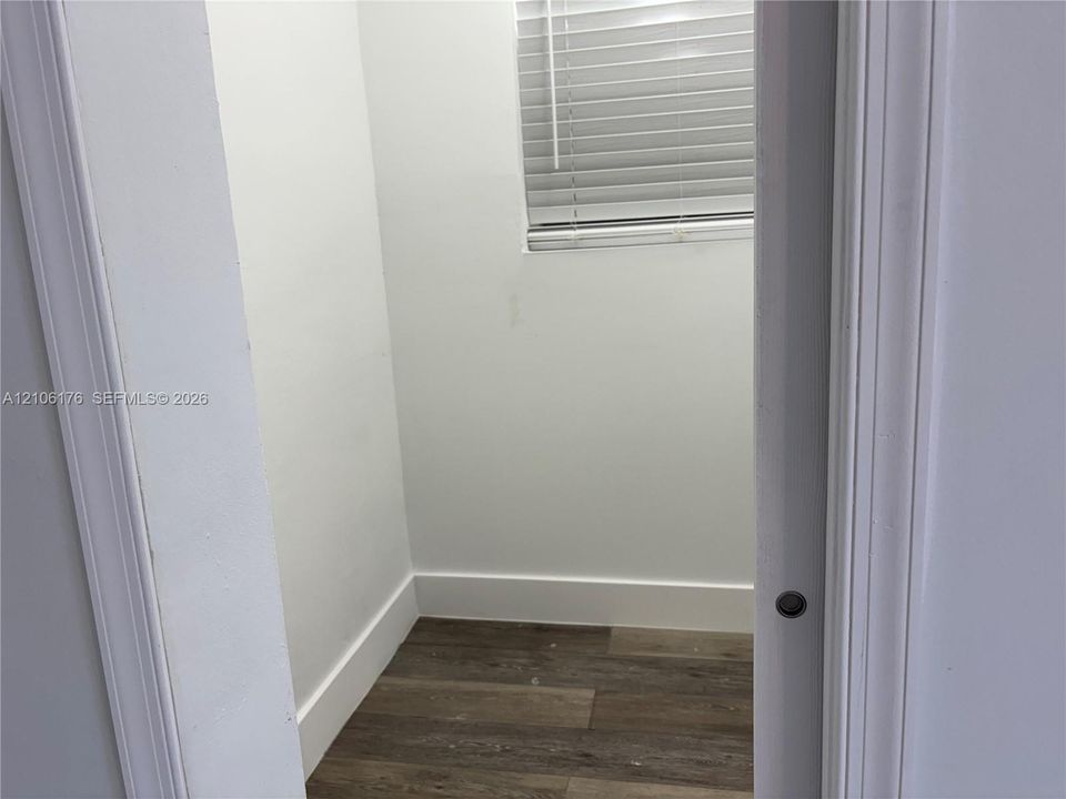 Enclosed area featuring wood-finish flooring, white walls, and a window with horizontal blinds