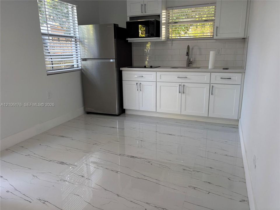Kitchen featuring white Shaker-style cabinetry, stainless steel refrigerator, white subway tile backsplash, and polished stone-finish tile flooring