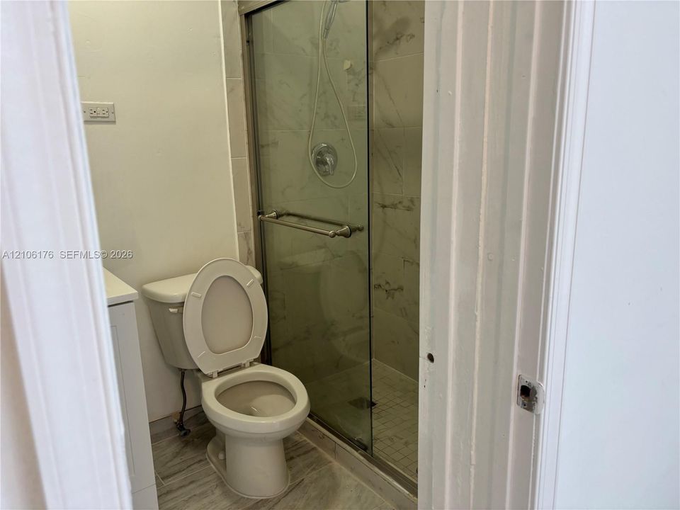 Walk-in shower with sliding glass doors, stone-patterned tile wall surround, and wood-finish flooring