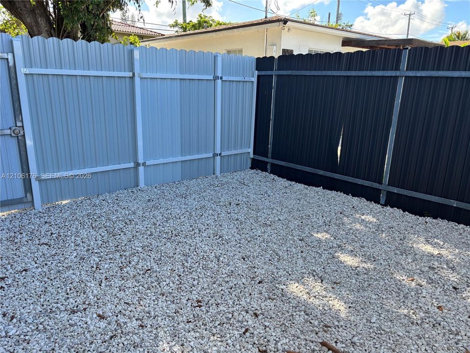 Ground-level exterior area featuring low-maintenance gravel surfacing enclosed by corrugated metal fencing