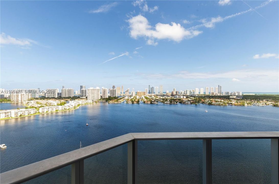 Balcony featuring a metal railing with glass panels, panoramic water expanse, and urban skyline backdrop