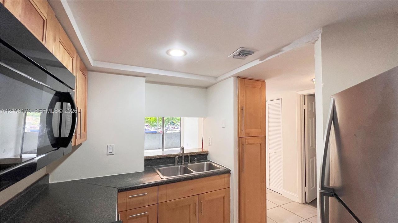 Kitchen featuring natural wood cabinetry, dark stone-finish countertops, stainless steel dual-basin sink with a chrome faucet, and stainless steel appliances