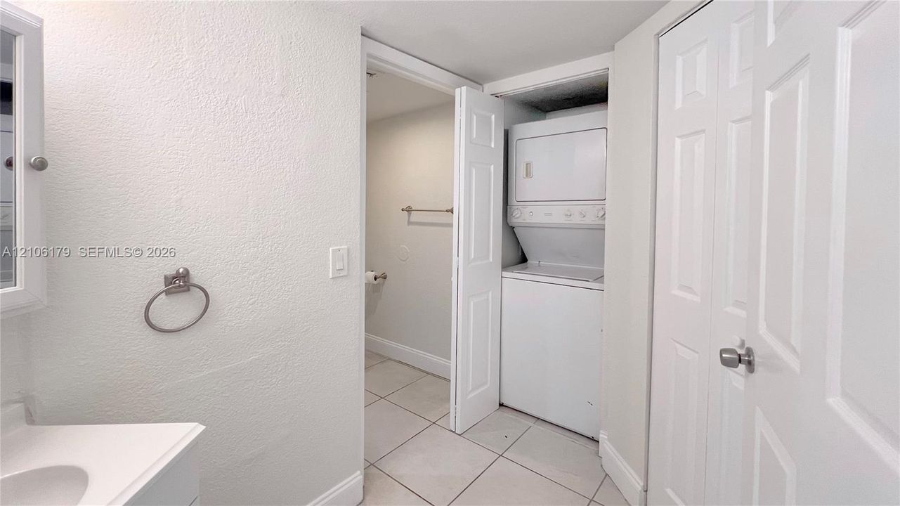 Laundry area featuring a stackable washer and dryer unit, neutral tile flooring, white six-panel interior doors, and polished chrome hardware