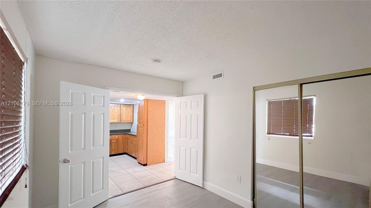 Interior space featuring light-toned flooring, wood-finish kitchen cabinetry, tile flooring in the kitchen, double-door entry, and sliding mirror-panel closet doors