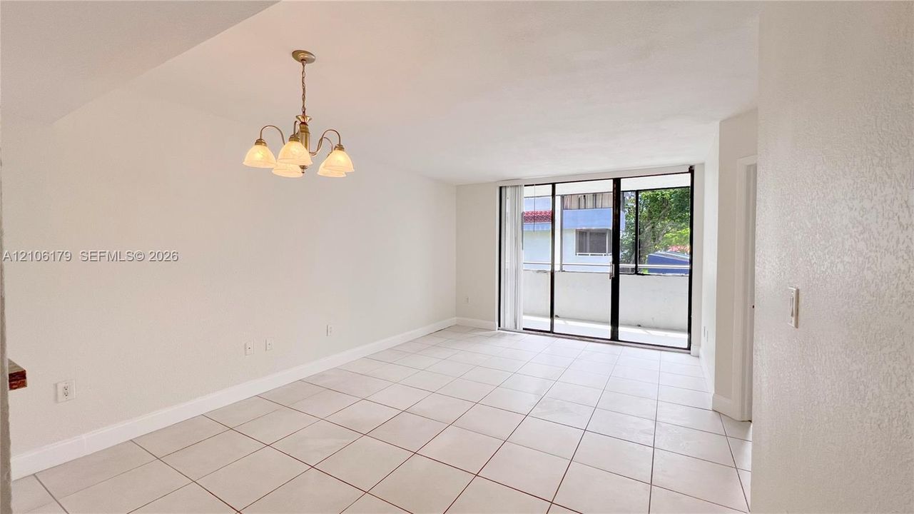 Bright interior space featuring light-colored floor tiling, a multi-arm chandelier, and floor-to-ceiling sliding glass doors leading to an exterior balcony