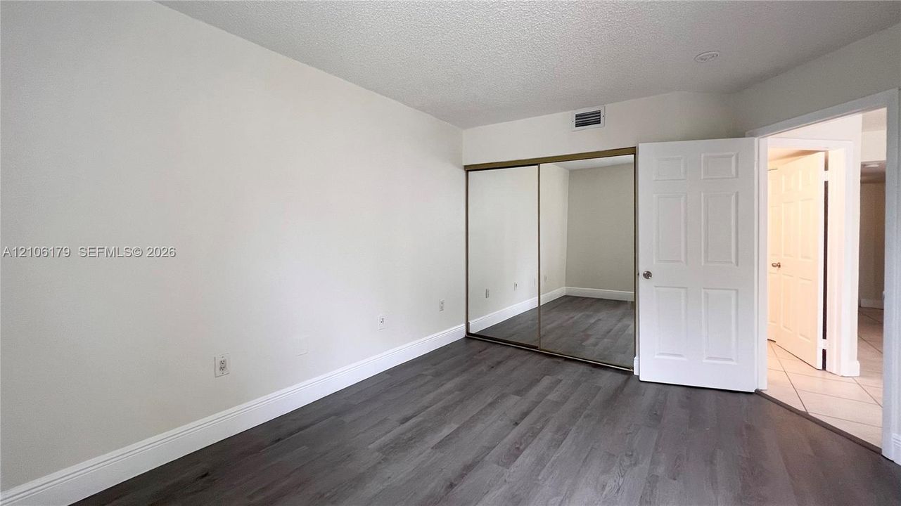 Room featuring wood-finish flooring, sliding mirror-panel closet doors, and six-panel interior door